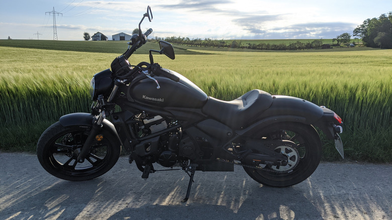 A Black Kawasaki Vulcan S parked on asphalt in front of a field of tall grass
