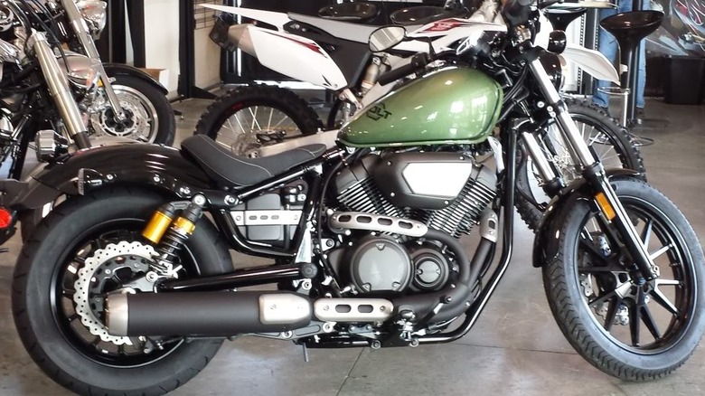 A green and black Yamaha Bolt R-Spec is parked indoors with other motorcycles in the background