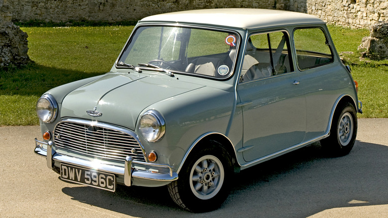 A front-quarter view of a green 1965 Austin Mini Cooper S parked in front of grass and a stone wall