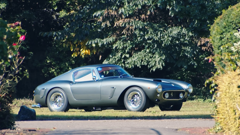 A front-quarter view of a gray 250 SWB Ferrari recreation parked on grass in front of trees