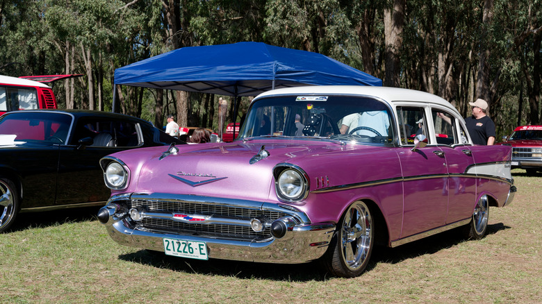 A front shot of a purple 1957 Chevrolet four-door sedan parked at an outdoor car show