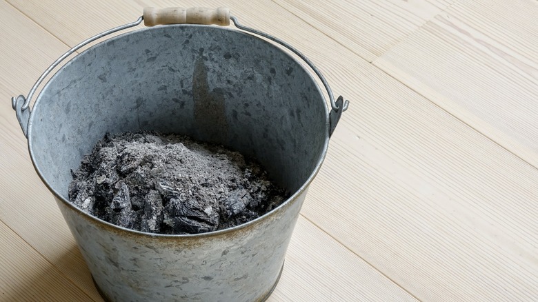 A bucket of wood ash sits on a wooden floor.