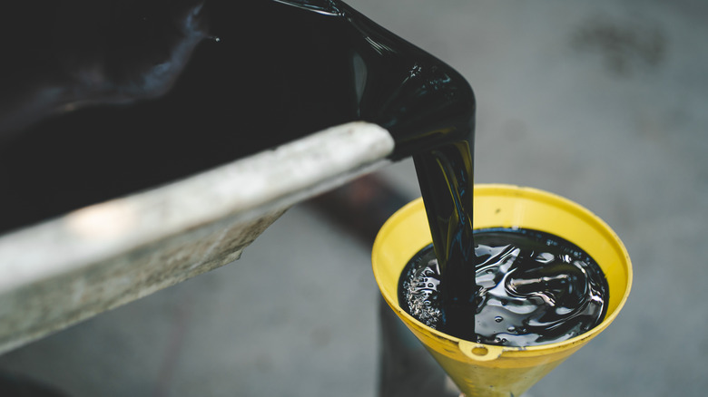 A stock image of an oil pan pouring oil into a yellow funnel during an oil change