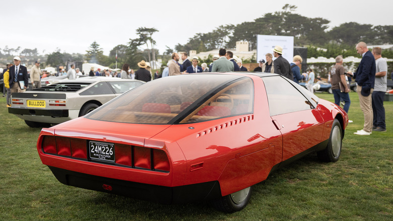 A red 1979 Ford on display at Pebble Beach Concours D'Elegance with numerous people and other cars in the background