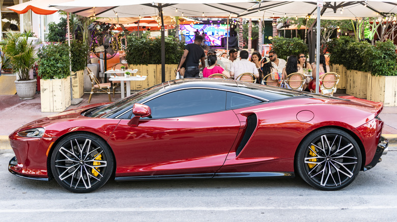 A red McLaren GT parked in front of a busy cafe.