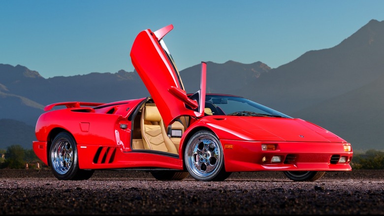 A red Lamborghini Diablo parked on pavement with the passenger door open in front of a distant mountain range