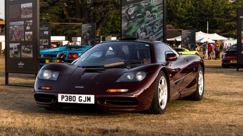 A brown McLaren F1 parked on a lawn at a car show with large display boards in the background