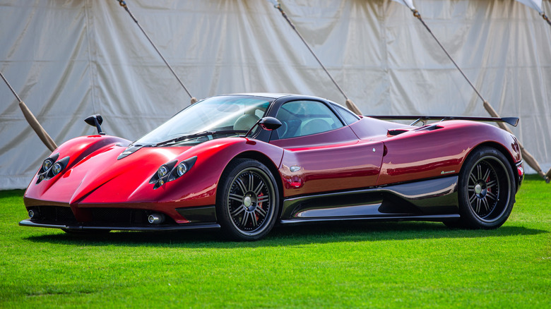 A red Pagani Zonda parked on a lawn with a large tent in the background