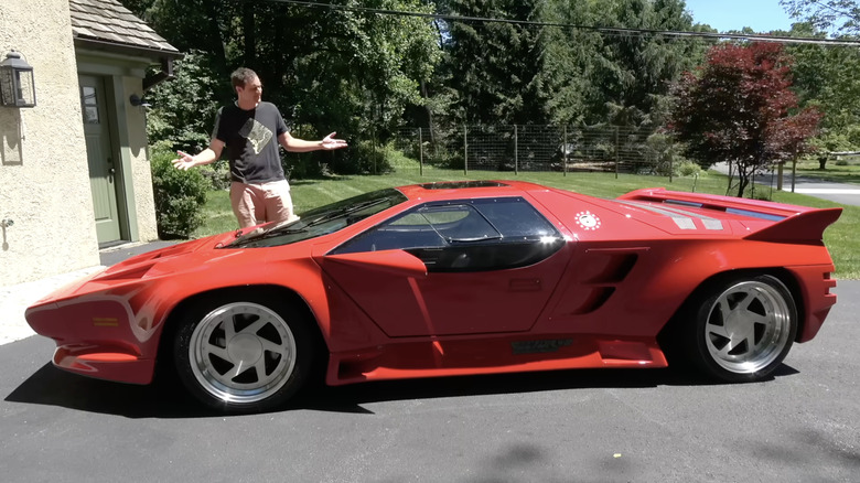 Daddy Doug DeMuro standing behind a red Wector V8 supercar.