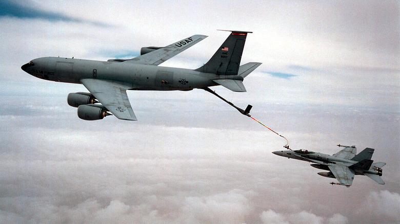 A mid-air refueling process taking place between a cargo plane and a fighter jet