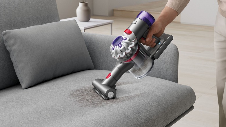 The Dyson Car and Boat handheld vacuum is used to remove hair from a gray couch.