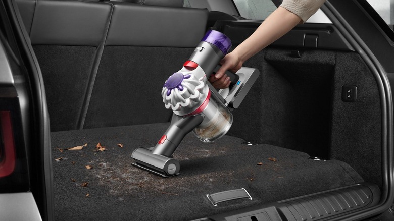 A Dyson handheld vacuum is used to clean up leaves and other debris in a vehicle cargo area.