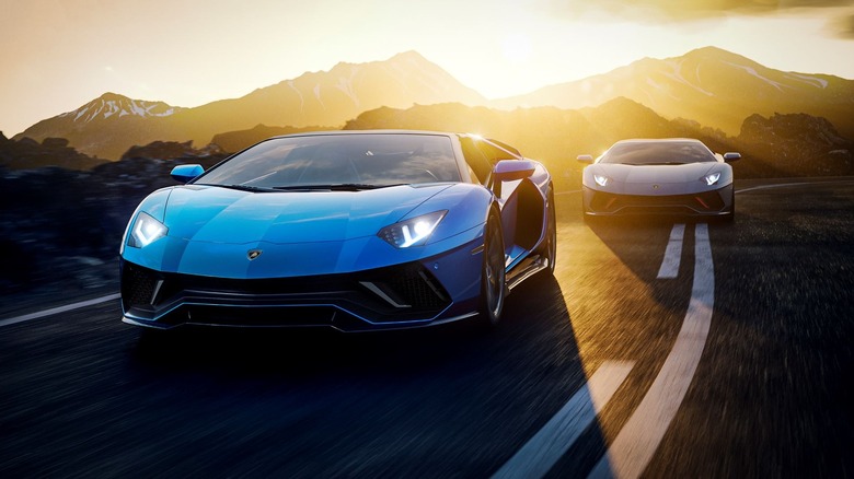 A pair of Lamborghini Aventador LP 780-4 Ultimae models driving on the road in with back-lit mountains