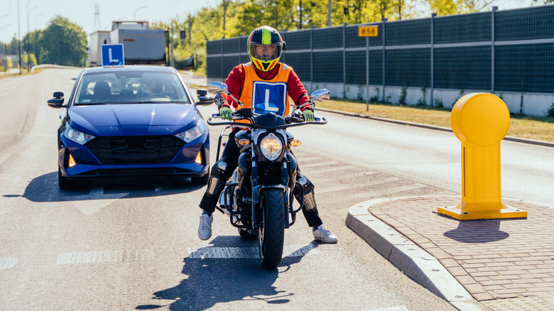 A motorcyclist and car with "L" (for "Learner") insignias at a crosswalk.