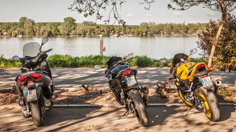 Three parked motorcycles facing a scenic lakeside.