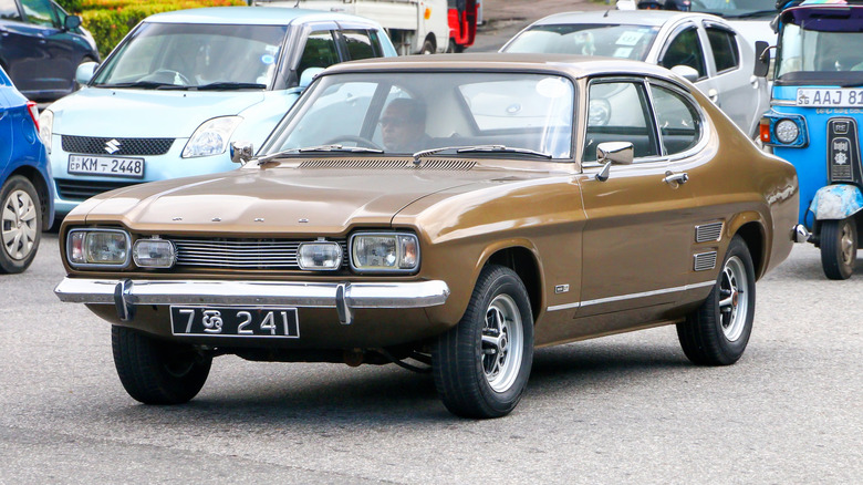 A brown Ford Capri Mk1 with someone inside it near other vehicles