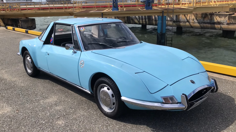 A blue Matra M530 car parked by water in an industrial area