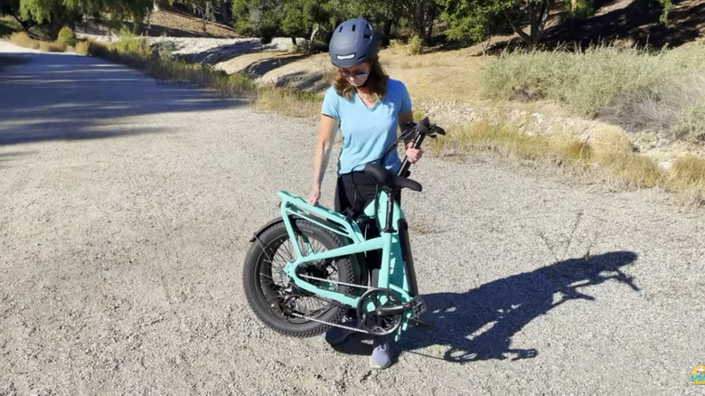 Woman lifting up folding e-bike on dirt road.