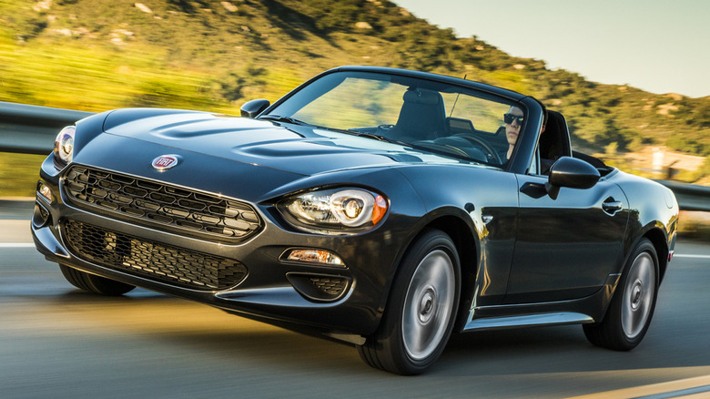 A black 2019 Fiat 124 Spider on the road with a hill behind it.
