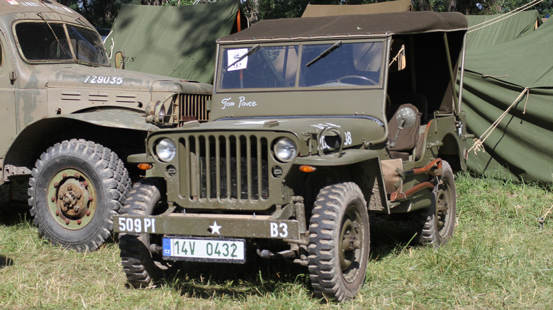A Willys Jeep military SUV parked on grass near other military equipment.
