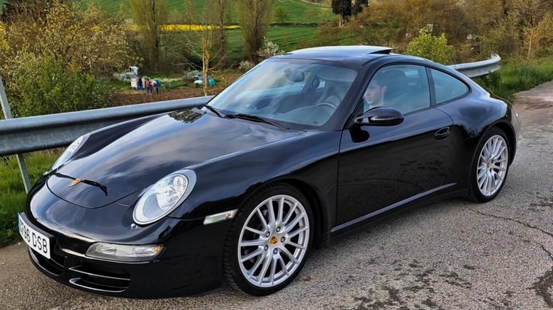 Driver's side view of a black 997 Porsche 911 Carrera 4 parked on a paved road next to a metal guardrail