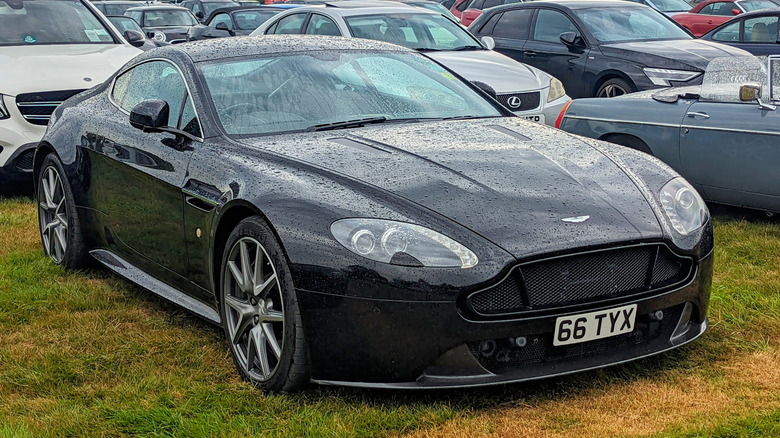 Front 3/4 view of a black 2012 Aston Martin V8 Vantage parked on grass