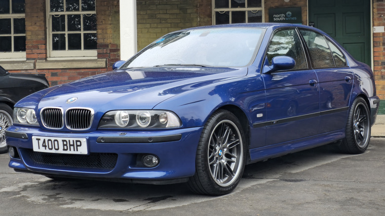 Front 3/4 view of a blue E39 BMW M5 parked in front of a building