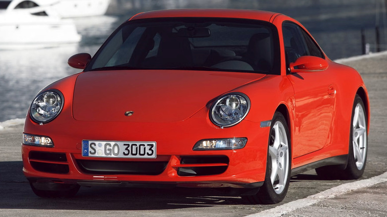 Front 3/4 view of a red 997 Porsche 911 Carrera 4 Coupe parked on a concrete surface with a body of water in the background