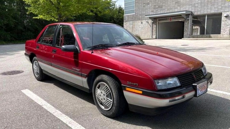 1987-1991 Pontiac Tempest parked on a paved surface with trees and a building in the background