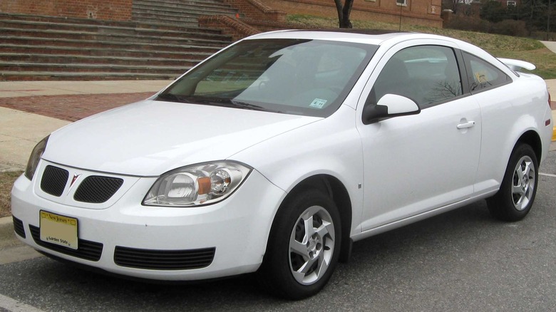 White Pontiac G5 Coupe parked on one side of street with buildings in the background