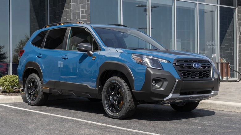 A blue Subaru Forester in a parking lot in front of a building.
