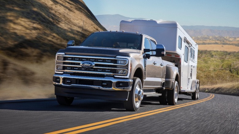 Gray 2023 Ford F Series Super Duty pickup truck seen in left front three-quarter view towing an RV trailer uphill