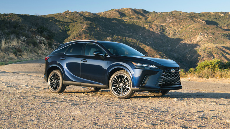 Dark blue 2024 Lexus RX 350 SUV seen in right front three-quarter view parked off-road with desert hills in background