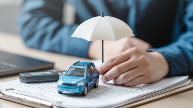 Person holds tiny umbrella over toy car