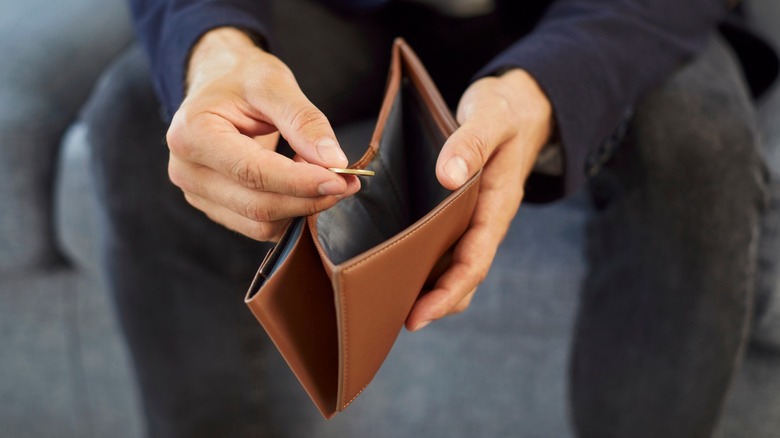 Man holding an empty wallet and one coin