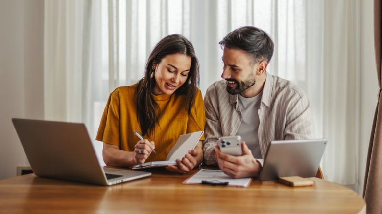 Young couple figuring out their finances, with laptops and smartphones.