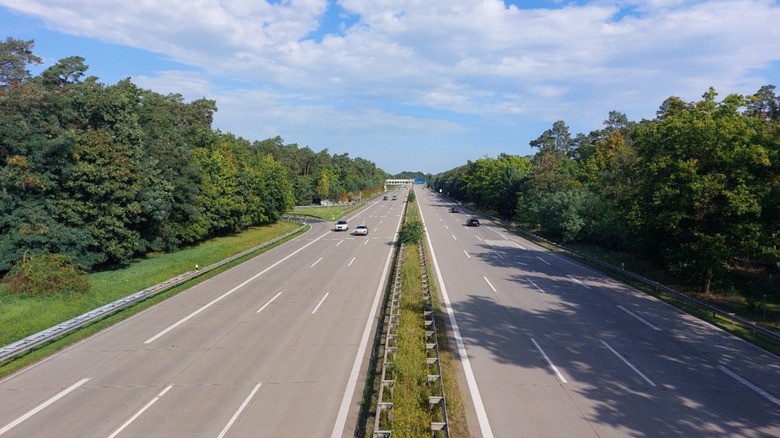 A relatively empty Autobahn in Germany, viewed from above the center median, with trees on either side the highway
