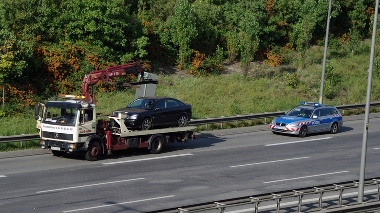 A broken down car being towed on the German Autobahn with a police car parked behind the tow truck