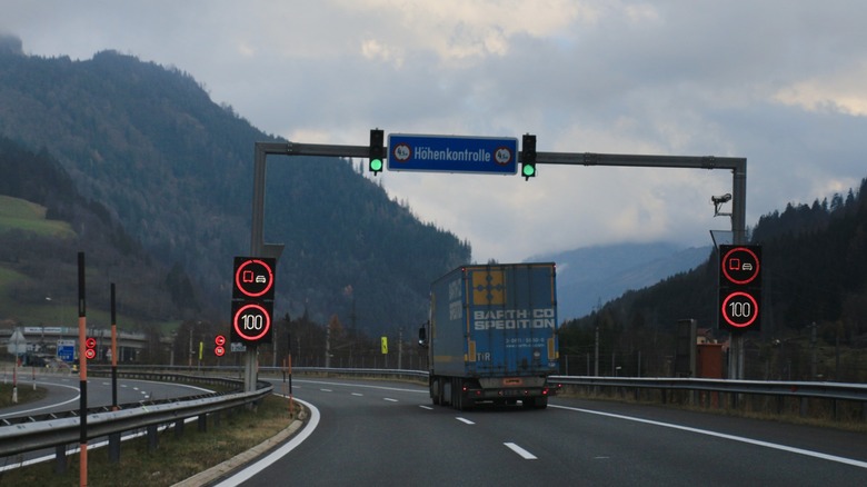 A moving truck on the German Autobahn driving beneath a gantry with speed limit signs and stop lights
