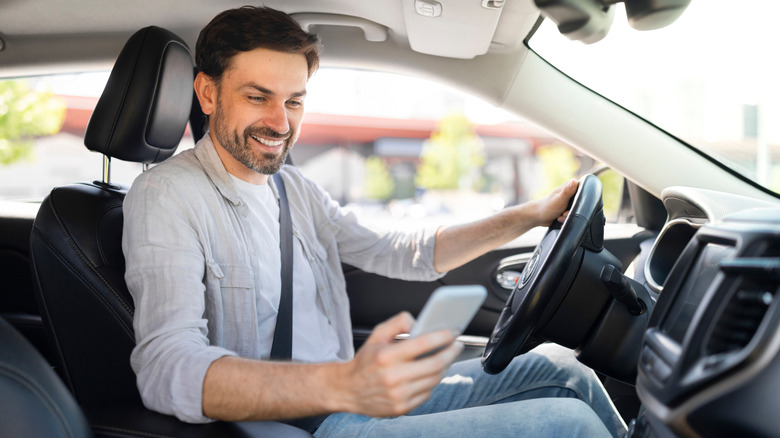 A person looking at a cellphone while at the wheel of a car