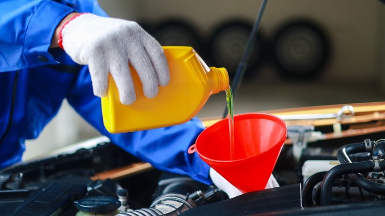 Mechanic pours engine oil into a car engine through a funnel