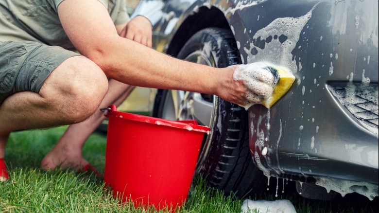 Man washes a gray car with a sponge and soapy water.