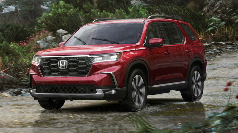 The front 3/4 view of a 2023 Honda Pilot Elite driving on an unpaved, rugged dirt road