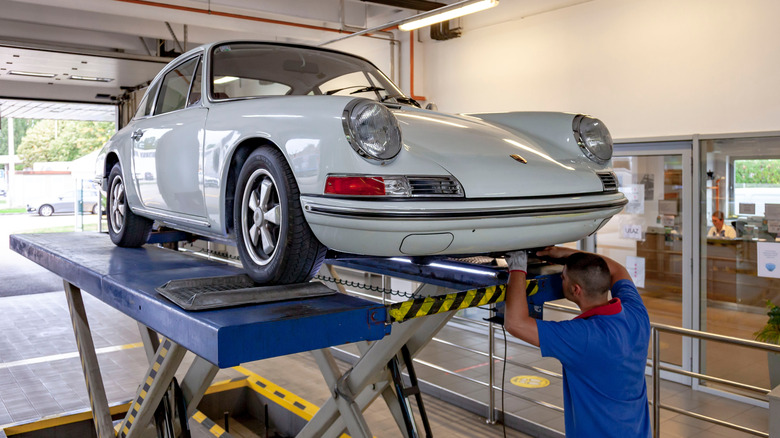 A vintage white Porsche on an inspection lift during a technical inspection.