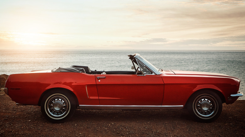 An early red Ford Mustang convertible, parked by the water at sunset.