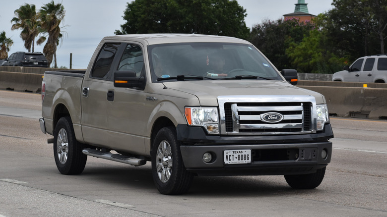 A metallic gold 2013 Ford F-150 truck driving on a highway.