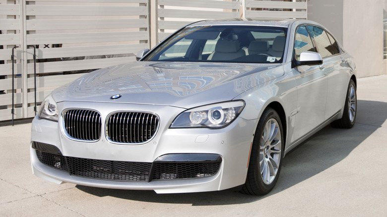 A silver 2012 BMW 7 Series parked near a fence.