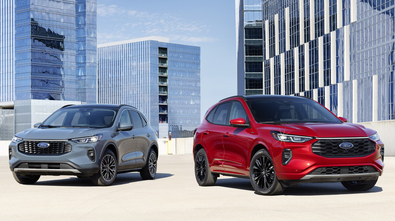 A vapor blue 2023 Ford Escape Plug-In Hybrid and a Rapid Red Ford Escape ST-Line Elite near some buildings
