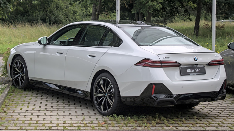 Rear 3/4 view of a 2024 BMW 540i xDrive Sedan parked on a paved surface with trees in the background