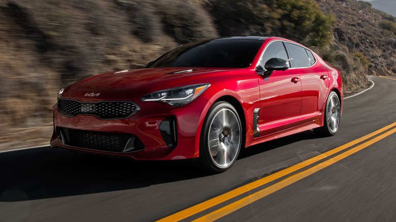 Front 3/4 view of a red Kia Stinger driving along a winding mountain road